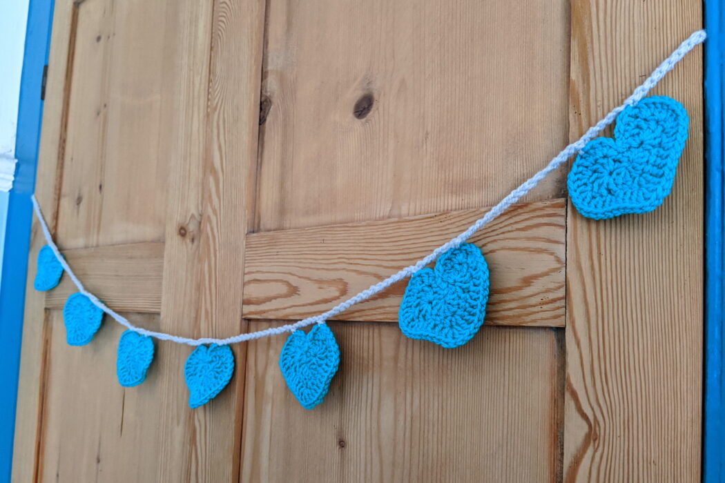 Turquoise crocheted heart bunting against a wooden door